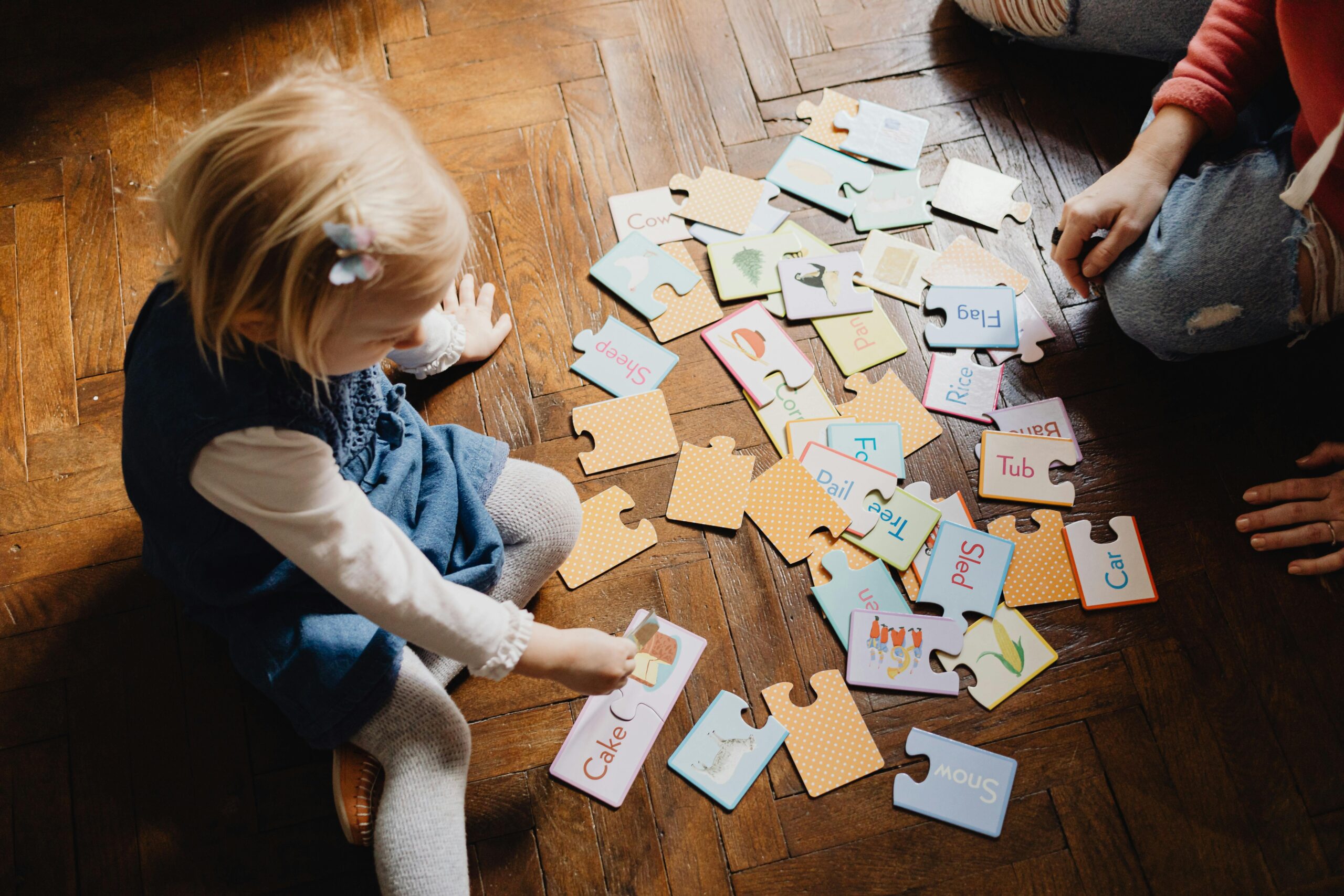 Toddler playing with word puzzle cards on a wooden floor